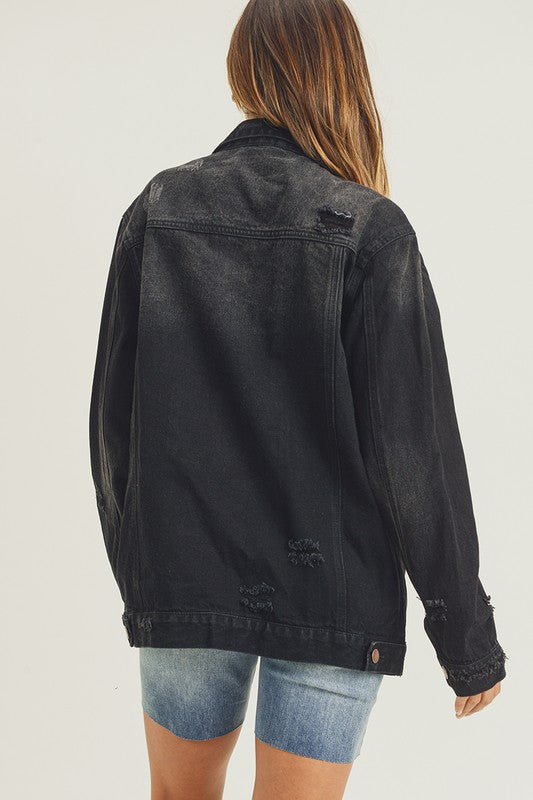 RISEN Black Vintage Wash Oversized Denim Jacket. Vintage wash black denim jacket with distressed details, button down front, button cuffs, front button pockets, additional side pockets, and a relaxed fit.