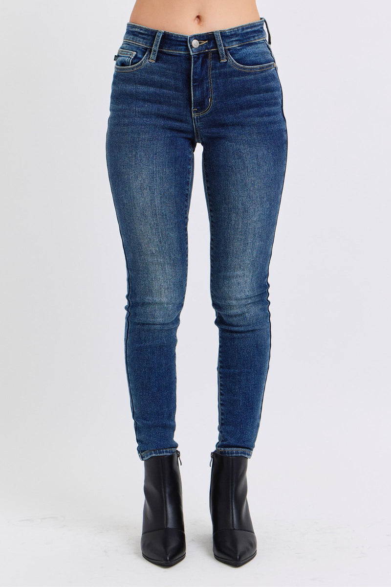 Judy Blue Mid Rise Thermal Skinny Jeans. Featuring Judy Blue stretch denim with a brushed thermal interior for an extra layer of warmth. Designed with a mid rise, dark wash, stitching on the back pockets, and no distressing.