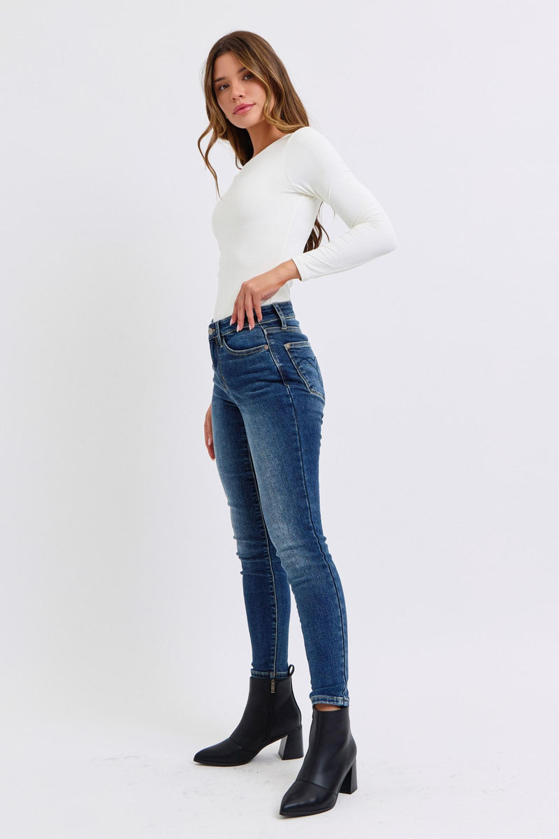 Judy Blue Mid Rise Thermal Skinny Jeans. Featuring Judy Blue stretch denim with a brushed thermal interior for an extra layer of warmth. Designed with a mid rise, dark wash, stitching on the back pockets, and no distressing. 