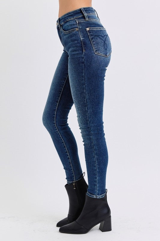 Judy Blue Mid Rise Thermal Skinny Jeans. Featuring Judy Blue stretch denim with a brushed thermal interior for an extra layer of warmth. Designed with a mid rise, dark wash, stitching on the back pockets, and no distressing. 